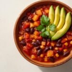 Vegan chili sin carne met kidneybonen, mais en avocado in een kom