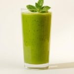 Groene smoothie met spinazie, mango en gember in een glas, gegarneerd met munt